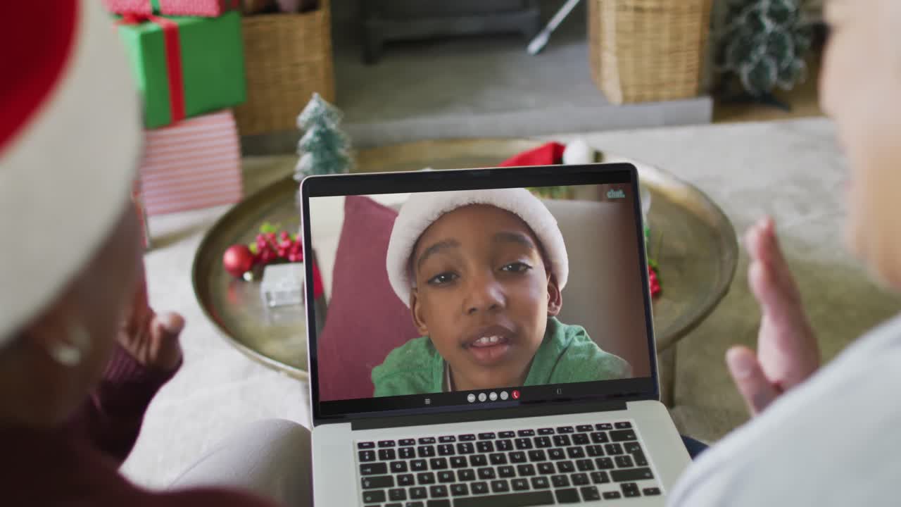 diversas amigas mayores agitando y usando una computadora portátil para una videollamada de navidad con un niño en la pantalla