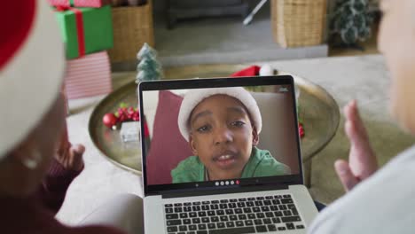 Diverse-senior-female-friends-waving-and-using-laptop-for-christmas-video-call-with-boy-on-screen