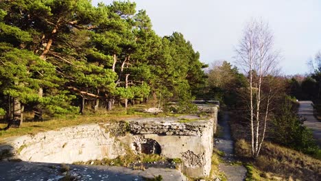 Aerial-view-of-concrete-Northern-fortification-ruins-covered-by-green-vegetation-and-trees-located-in-Liepaja,-Latvia-in-sunny-day,-wide-angle-establishing-drone-shot-moving-backwards