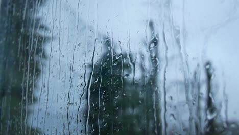 Rainy-storm-droplets,-moody-weather-fall-down-window-glass-closeup-bokeh