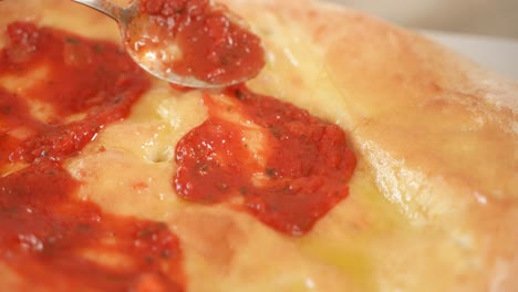 hand uses metal spoon to apply tomato sauce on pizza dough, slow motion