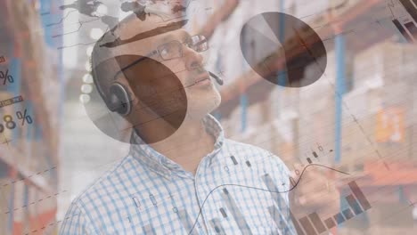 Animation-of-Caucasian-man-talking-with-headphones-in-warehouse-area-over-statistics-