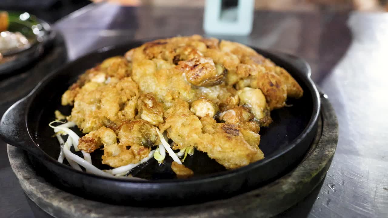 Golden oyster pancake sizzles on hot pan, garnished with bean sprouts, vibrant street food setting