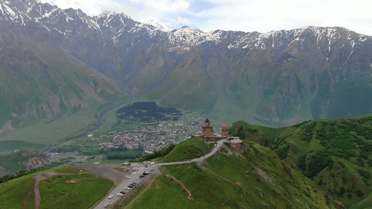 vista aérea de drones en georgia volando sobre la iglesia ortodoxa de la trinidad de gergeti en kazbegi rodeada de montañas verdes valle con picos nevados
