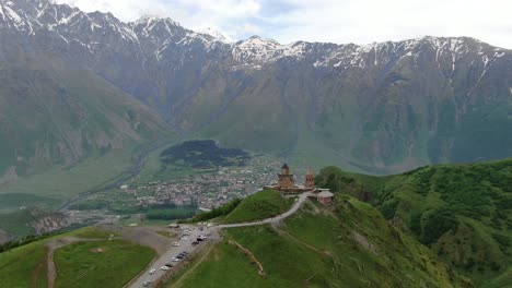 vista aérea de drones en georgia volando sobre la iglesia ortodoxa de la trinidad de gergeti en kazbegi rodeada de montañas verdes valle con picos nevados