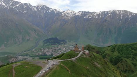 drone aerial view in georgia flying over gergeti trinity orthodox church in kazbegi surrounded by green mountains valley with snowed peaks