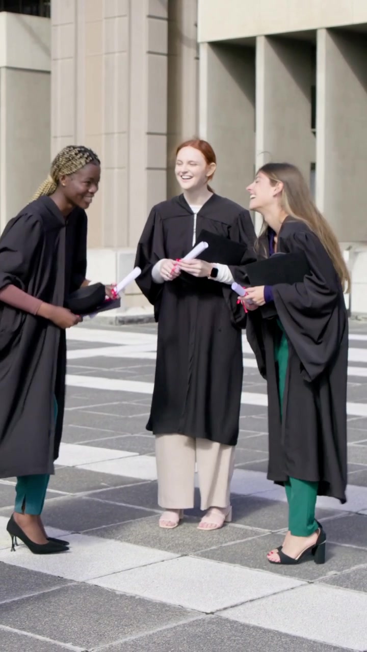 Vertikal video: Løfter huen, en kandidat til venstre, der præsenterer, medstuderende fejrer med diplomer i kåber på pladsen