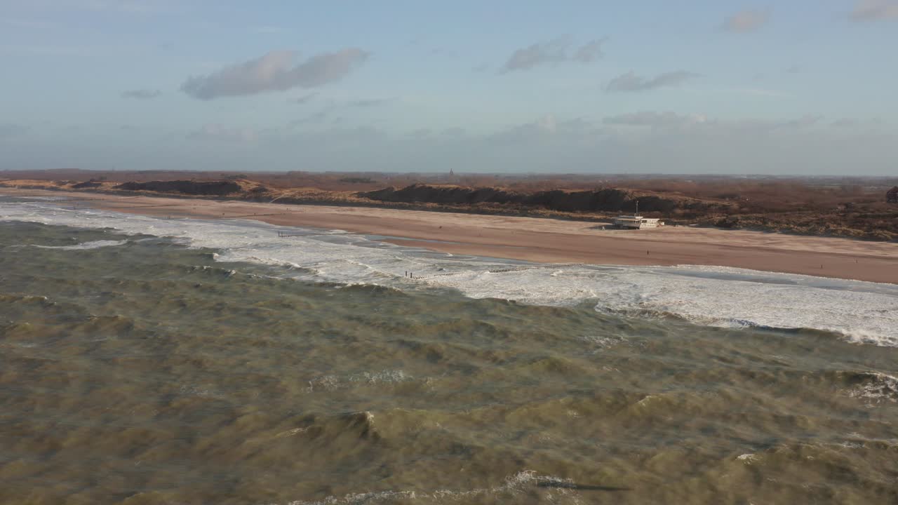 Revealing drone shot of a quiet beach with a kitesurfer jumping in the foreground
