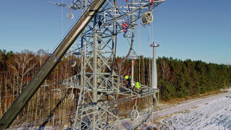 carretilla aérea que revela a dos electricistas que trabajan en el mantenimiento de una torre de alta tensión en un bosque nevado