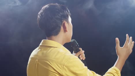 close up back view of young asian boy holding a microphone and singing on the white smoke black background