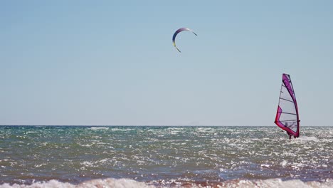 Windsurfer-Mit-Kitesurfer-Im-Hintergrund