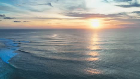 Fixed-drone-shot-of-a-beautiful-golden-sunset-over-open-blue-ocean-to-the-horizon-with-gently-wrapping-waves-and-whitewater