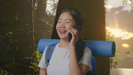 close up of asian female hiker with mountaineering backpack smiling and talking on smartphone while exploring forest nature