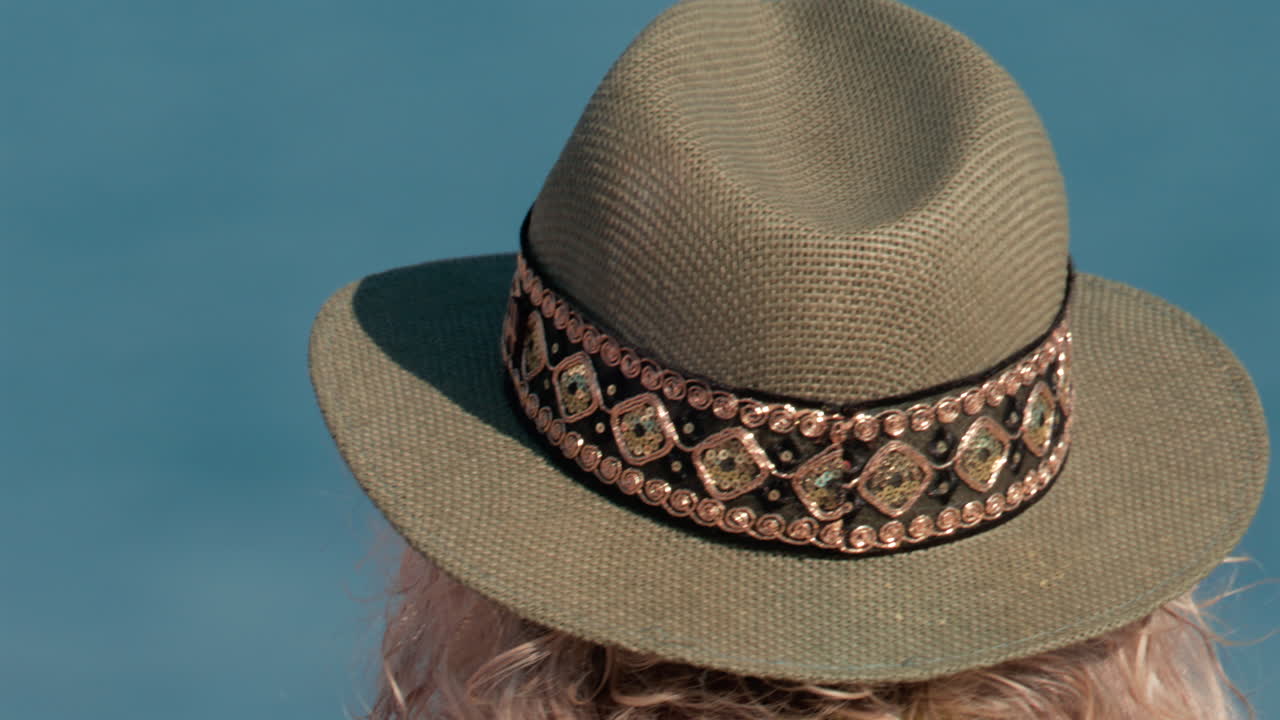 Close up of a decorated sun hat worn by a person facing the calm blue water