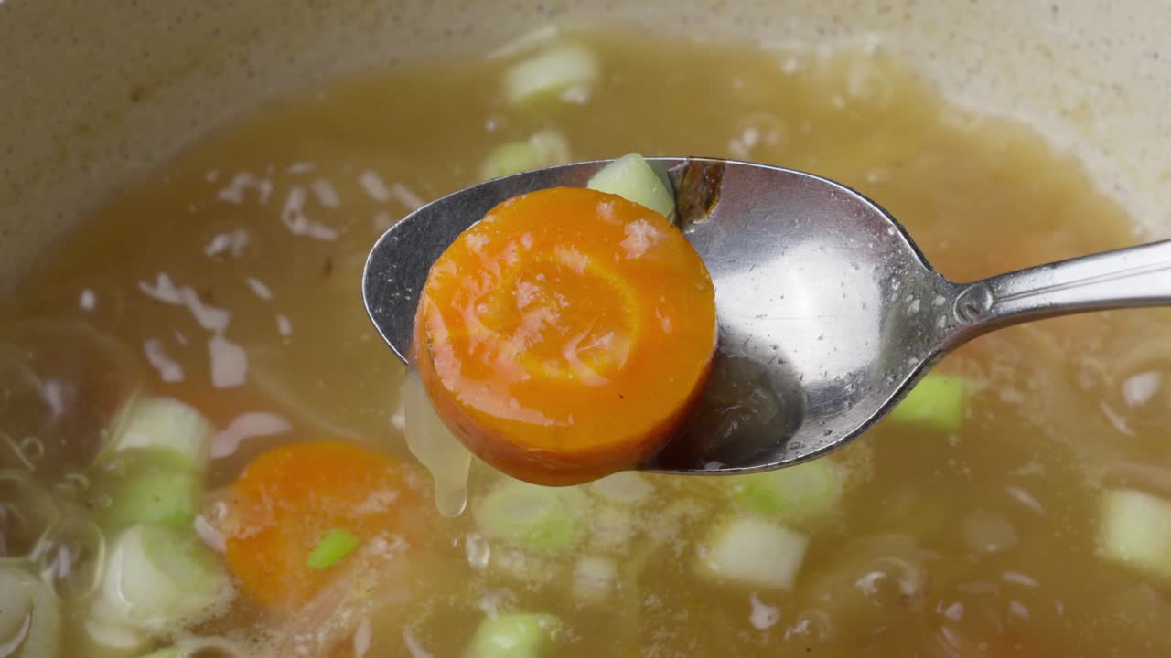 Primo piano, zuppa di verdure bollente con ingredienti freschi e carota su un cucchiaio.