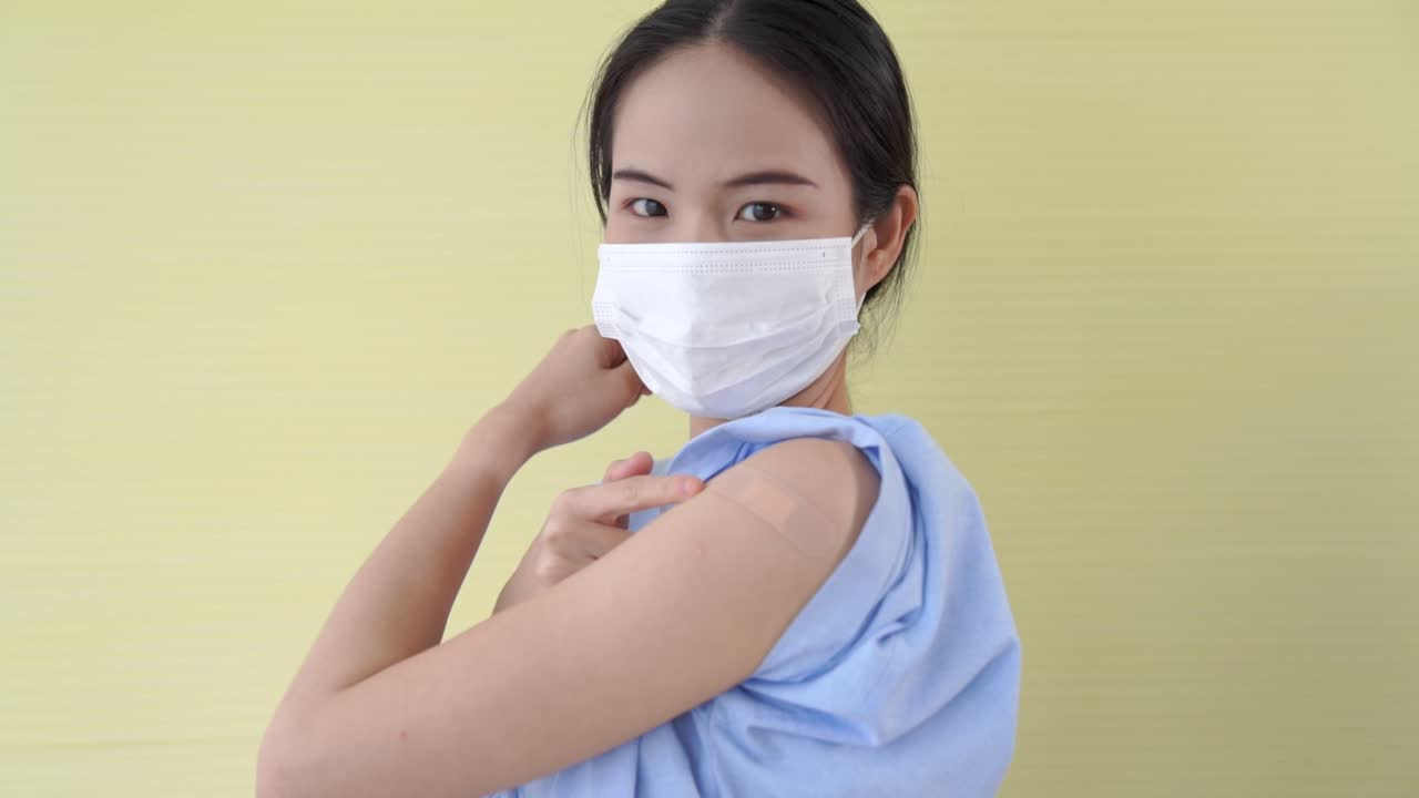 Young Asian woman showing COVID-19 vaccine bandage merrily