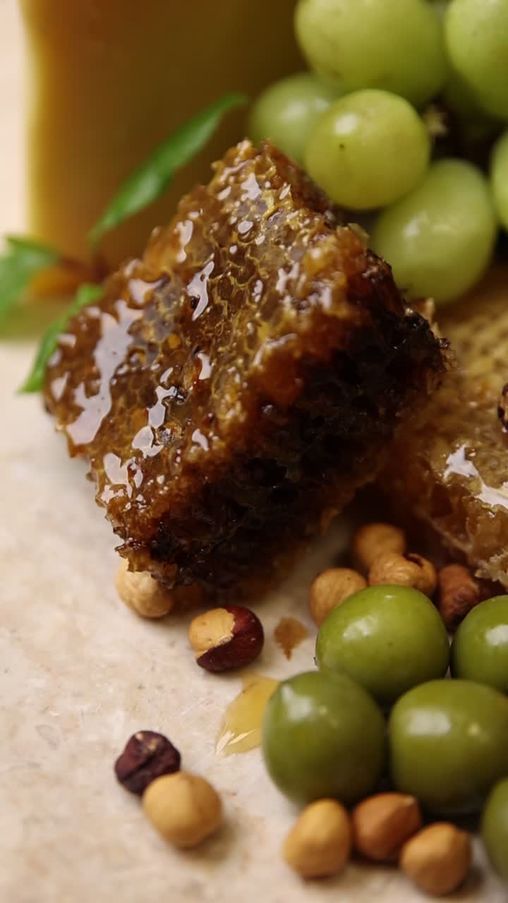 Close-up of Honeycomb with Dripping Honey, Grapes, Olives, and Hazelnuts