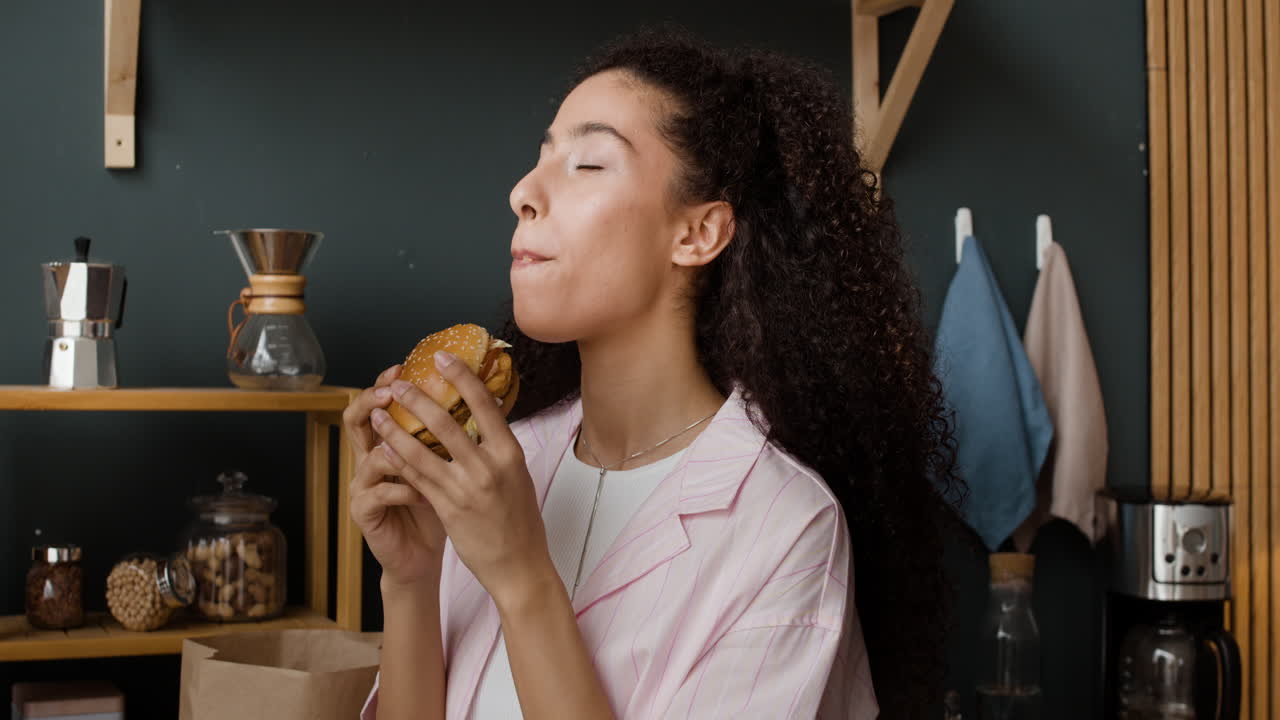Young woman enjoying a burger in the kitchen