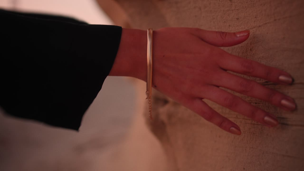 Girl waving her hand over a rock in the desert wearing a black abaya and gold hand bracelet while a sunset close up shot of fossil dunes