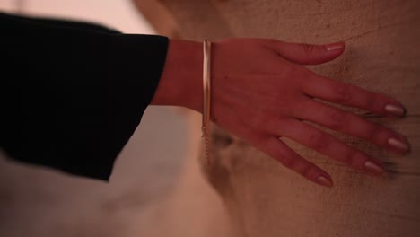 Girl-waving-her-hand-over-a-rock-in-the-desert-wearing-a-black-abaya-and-gold-hand-bracelet-while-a-sunset-close-up-shot-of-fossil-dunes