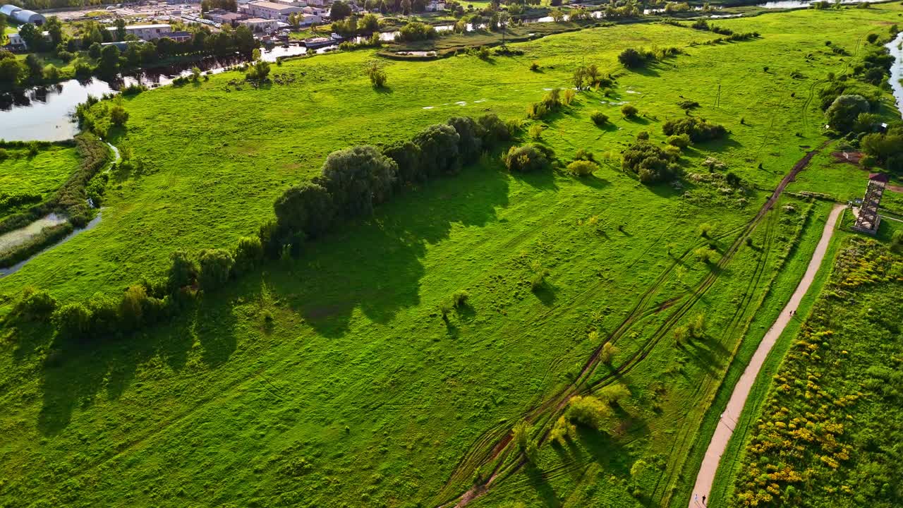 Riverside green meadow with footpath trail curving into distance on sunny summer day