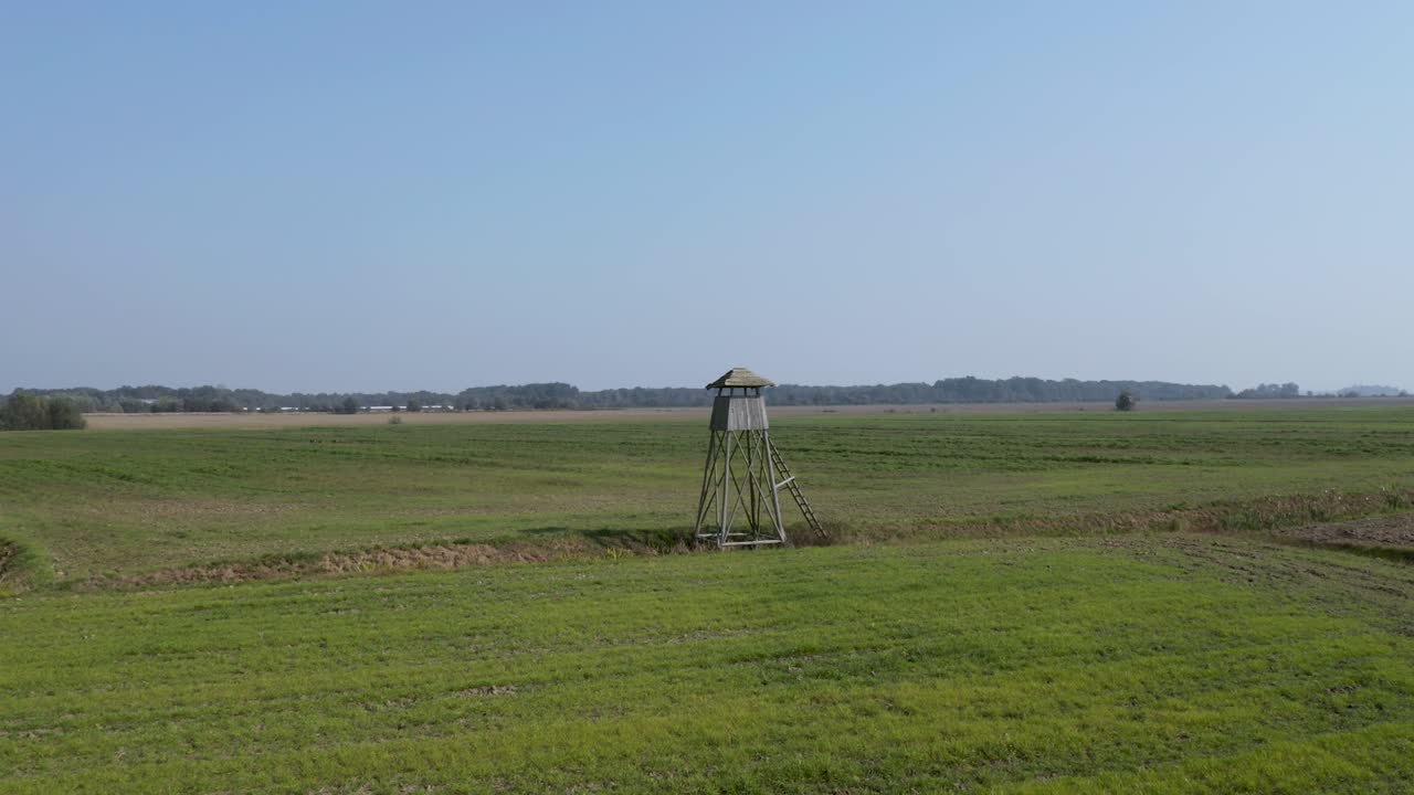 Drone footage flying near a wooden hunting lookout in the middle of crop fields on farmland in rural Slovenia