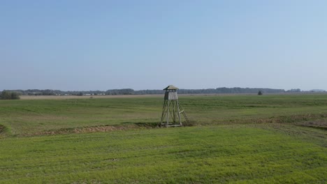 Drone-footage-flying-near-a-wooden-hunting-lookout-in-the-middle-of-crop-fields-on-farmland-in-rural-Slovenia