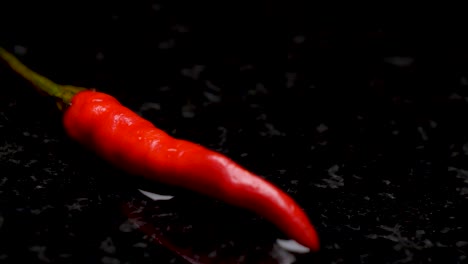 moist red chilli on a black background tile, sliding shot