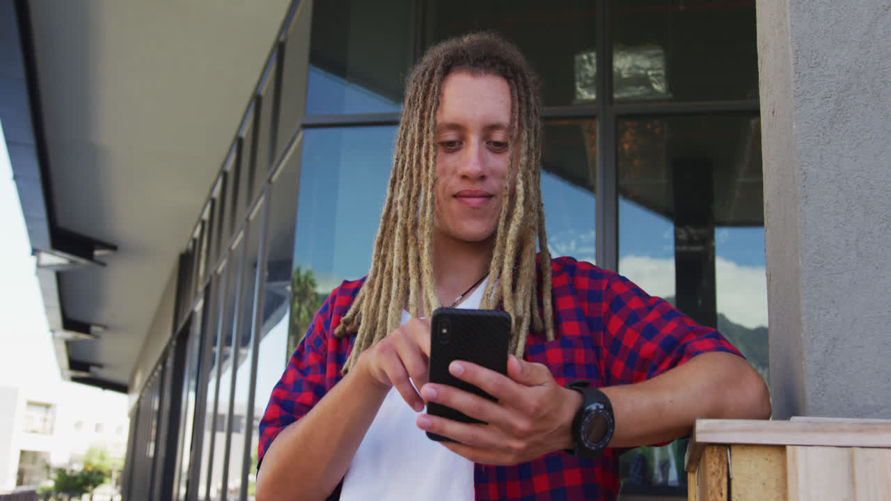Mixed race man with dreadlocks sitting at table outside cafe using smartphone