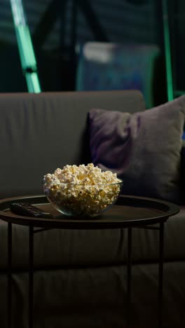 vertical video bowl of popcorn on table in empty neon lit cozy residential interior
