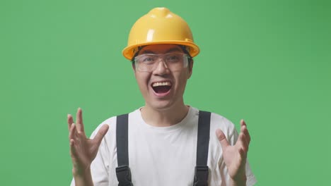 close up of asian man worker wearing goggles and safety helmet smiling and saying wow while standing in the green screen background studio