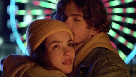 Tender-couple-hugging-against-ferris-wheel.-Man-touching-woman-on-urban-street.