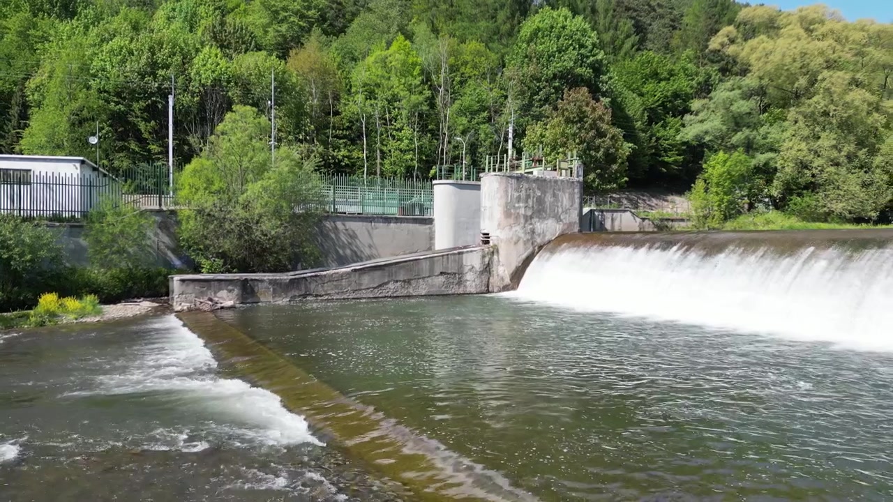 Paesaggio estivo soleggiato ripreso da drone che mostra il fiume Koszarawa, acqua che scorre su uno sbarramento, strutture idrotecniche, riva rocciosa, vegetazione lussureggiante e dintorni naturali tranquilli.