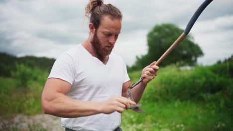 Man-Standing-Outdoor,-Sharpening-Rusted-Scythe-With-Whetstone