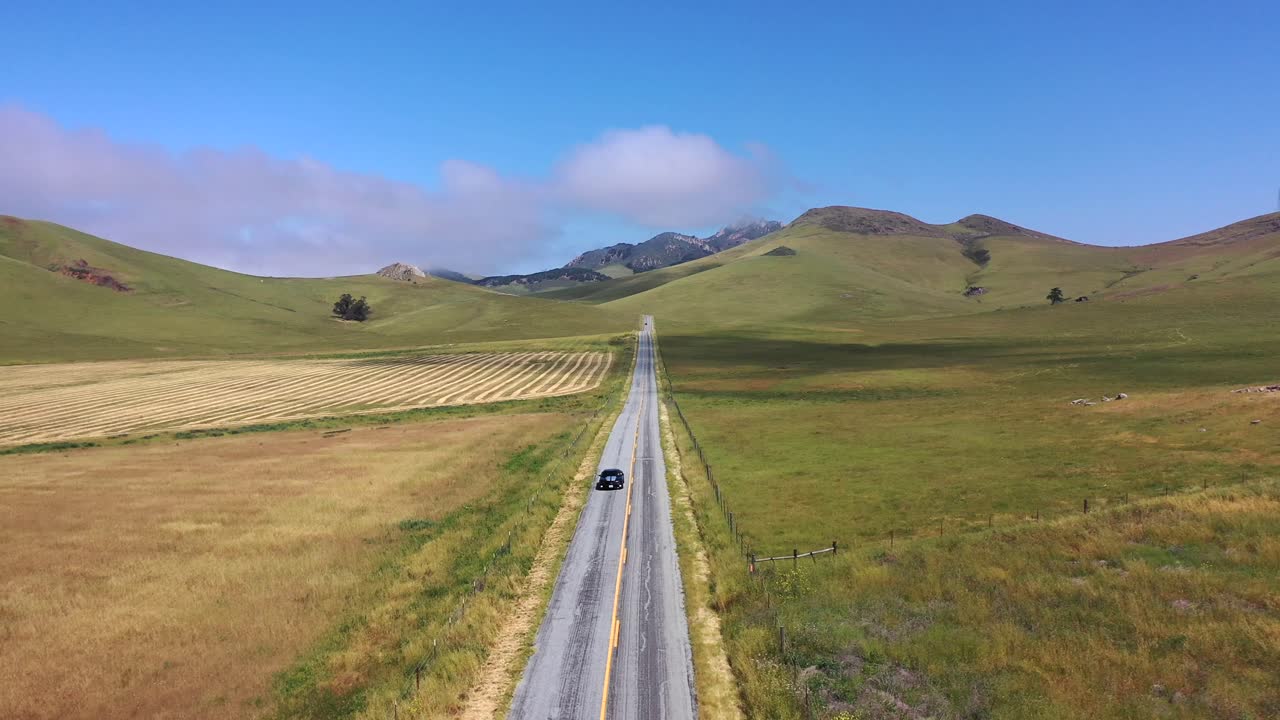 Car Driving Through Empty Road Between Grassy Fields At Daytime In San Luis Obispo, California. - aerial
