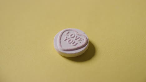 hand picking up heart candy with love you message on yellow background