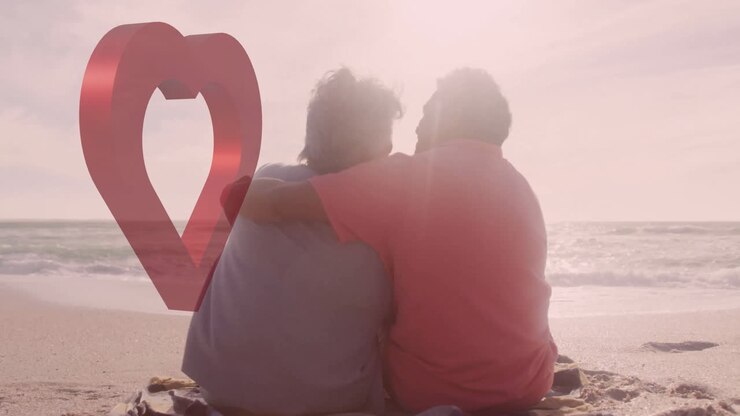 Due persone sedute in spiaggia con animazione a cuore sopra di loro