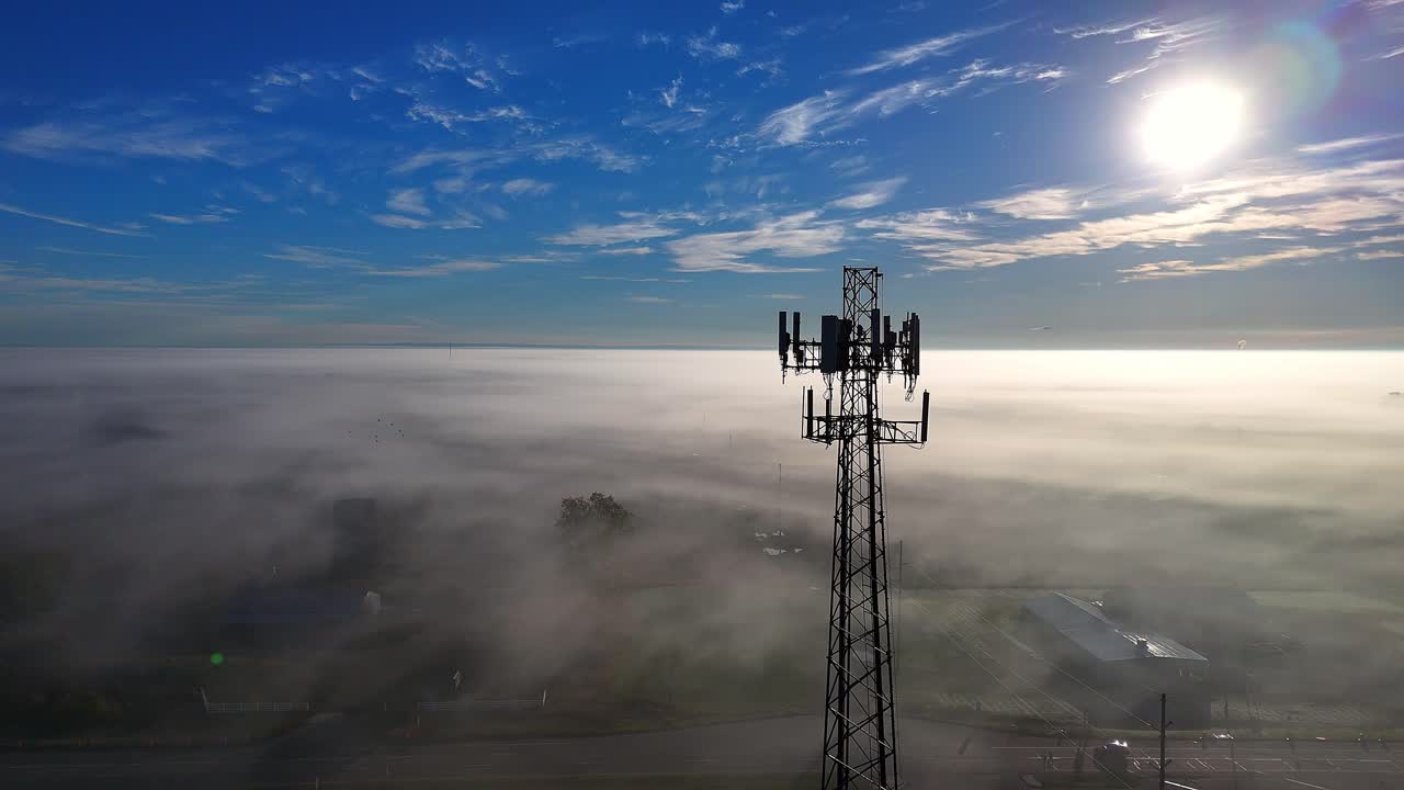 Torre di telecomunicazioni che trasmette segnali sopra uno strato di fitta nebbia sotto un cielo limpido in vista aerea.