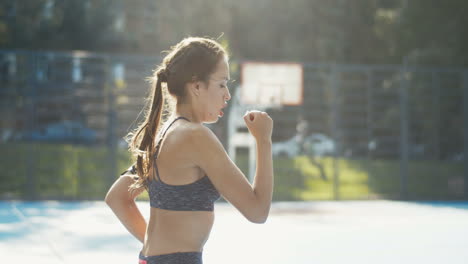 side view of a sporty woman running in place at outdoor court on a summer day