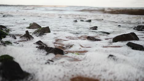 Nahaufnahme-Von-Strandwellen,-Die-Gegen-Die-Algenfelsen-Schlagen-Und-An-Einem-Windigen-Abend-Zurückweichen-Und-Einen-Schwall-Erzeugen