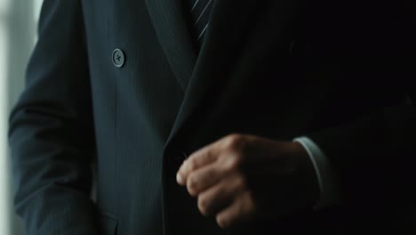 confident businessman buttoning or adjust classic blue suit near window in hotel room at the morning. handsome man wearing a nice suit on wedding day.