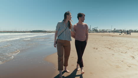 a happy couple walking down the beach barefoot holding hands