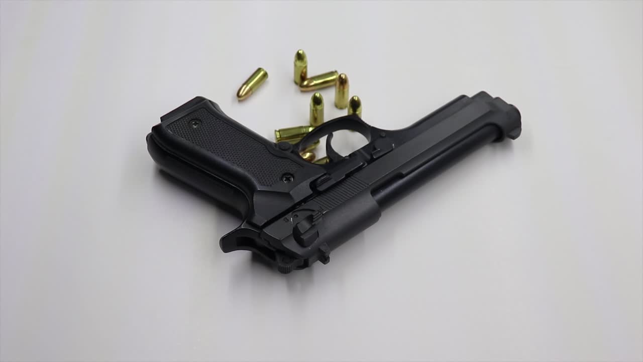 색 테이블 위에 9mm 탄약을 은 검은색 총을 아내고 있습니다.