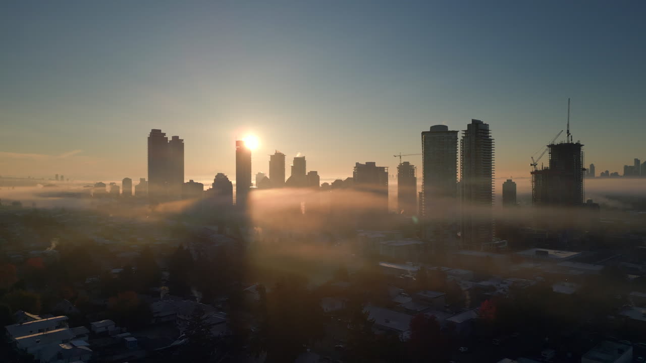 Arranha-céus com o nascer do sol atravessando-os em uma cidade com neblina