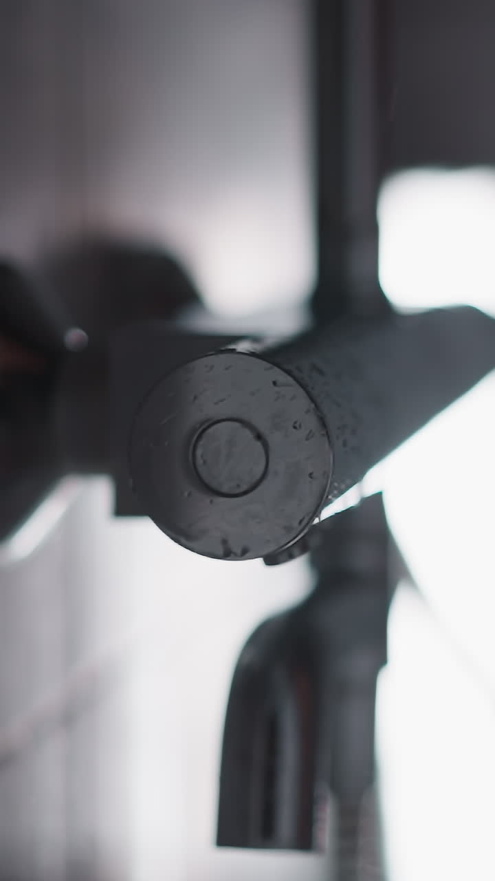 강한 압력으로 샤워 객실에서 물이 흐릅니다. 은 뜨거운 물의 강한 압력이 타일 벽이 있는 어두운 회색 욕실에서 금속 반이는 샤워에서 흐릅니다.