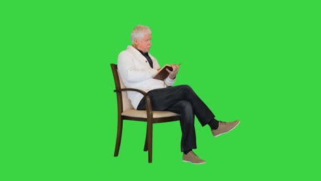 hombre mayor estudiando un libro sentado en una silla en una pantalla verde, clave de croma