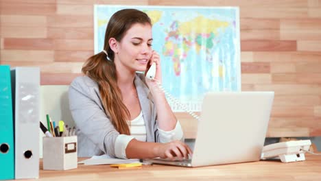 Casual-businesswoman-using-laptop-and-having-a-phone-call