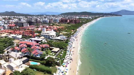 escena aérea de playa turística en florianópolis con muchos hoteles casas y edificios frente al mar con muchos alojamientos temporada de verano y arena con mucha gente tomando el sol en jurere internacional