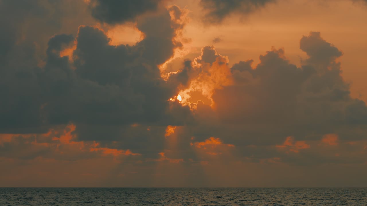 Bright sun rays shine through dramatic clouds during a vibrant orange sunset above the ocean. Stunning seascape with visible light beams, warm colors, and a calm horizon