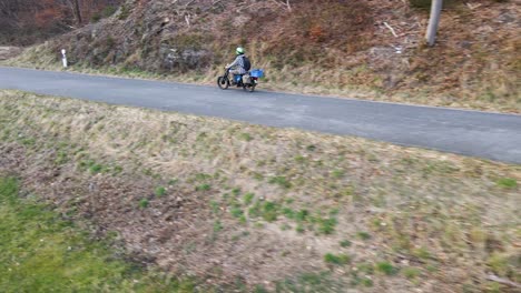 person on a moped driving along a narrow country road while a car passes by